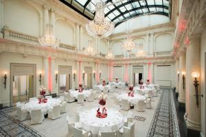 Großes Zimmer mit weißen Tischen und Kronleuchtern. in der Unterkunft Rocco Forte Hotel De Rome in Berlin