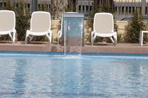 two white chairs and a fountain in a pool at Hotel Castilla Alicante in Alicante
