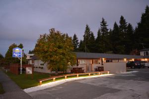 een parkeerplaats met een gebouw met een bord en een boom bij Amber Court Motel in Te Anau