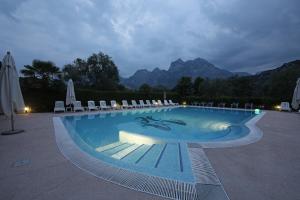 ein großer Pool mit Stühlen und Bergen im Hintergrund in der Unterkunft Hotel Villa Verde in Nago-Torbole