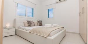 a white bedroom with a bed and two windows at Sea View Villa Paralimni in Paralimni