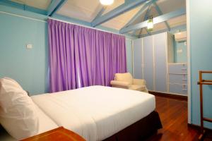 a bedroom with a bed and a chair and purple curtains at Kapitan Lodge in Port Dickson