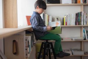 a young boy sitting on a stool with a book at INTRO Tamagawa in Kanazawa