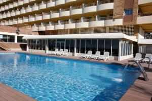 a large swimming pool with chairs and a building at Hotel Castilla Alicante in Alicante