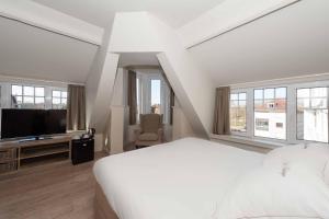 a white bedroom with a large bed and a television at Hotel Heritage in De Haan