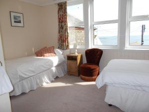 a bedroom with two beds and a chair and windows at Glenleigh Bed and Breakfast in Marazion