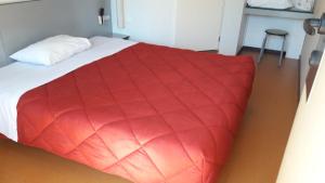 Un dormitorio con una manta roja sobre una cama. en Premiere Classe Limoges Nord, en Limoges