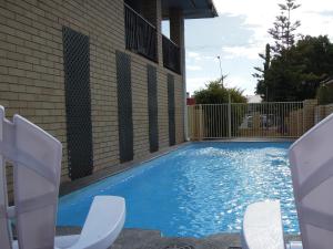 a swimming pool with two chairs in front of a building at Jackaroo Apartments in Moree