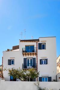 a white building with blue windows and a tree at Santina in Castellammare del Golfo