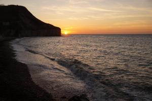 a sunset over the ocean with a rocky beach at Le Clos Saint Jean in Sainte-Honorine-des-Pertes