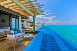 a hotel room with a pool, chairs, and a balcony at Velassaru Maldives in South Male Atoll