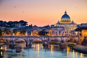 a bridge over a river with a building and a cathedral at L'obelisque maison de luxe in Rome
