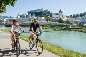 Ein Mann und eine Frau, die Fahrrad fährt, neben einem Fluss in der Unterkunft Hotel Alt-Oberndorf in Oberndorf bei Salzburg