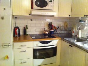 een keuken met een fornuis, een wastafel en een magnetron bij Lägenhet Elofstorps Gamla Missionshus in Kristinehamn