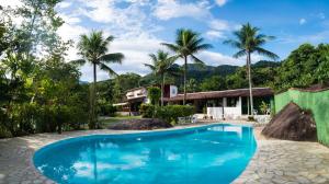 a swimming pool in front of a house with palm trees at Pousada Tarituba in Paraty