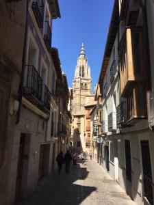 un grupo de personas caminando por una calle con una torre del reloj en Apartamentos Catedral Escalinata, en Toledo