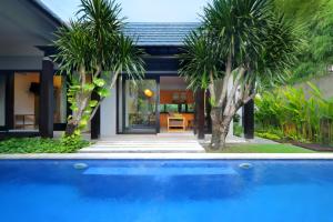 une piscine en face d'une maison avec des palmiers dans l'établissement The Jineng Villas by Ekosistem, à Seminyak