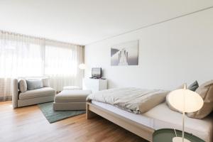 een witte slaapkamer met een bed en een stoel bij Serviced Apartments Haus 1 in Uzwil