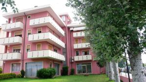 różowy budynek z drzewami przed nim w obiekcie Residence Eur w mieście Sottomarina