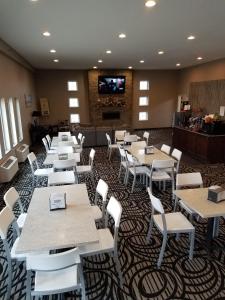 un restaurante con mesas, sillas blancas y TV en Okoboji Inn & Suites, en Milford