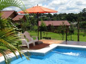 a swimming pool with an umbrella and two chairs and a table and an umbrella at Cabañas Doralia in Oberá