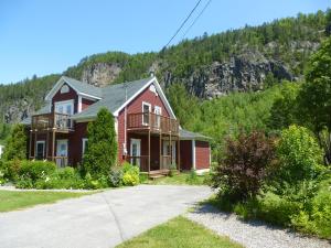 a large red house with a mountain in the background at B&B Les Deux Pignons in Petit-Saguenay