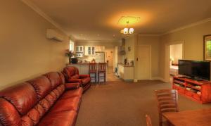 a living room with a brown leather couch and a kitchen at Grace's Spa Cottage in Smithton