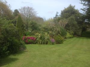 a garden with green grass and flowers and bushes at La Michele in St Martin Guernsey