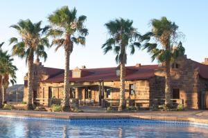 a house with palm trees in front of a swimming pool at Duwisib Guest Farm in Duwisib