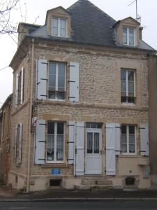 ein altes Backsteingebäude mit weißen Fensterläden in der Unterkunft Relais du Cap romain in Saint-Aubin-sur-Mer