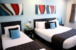 two beds in a hotel room with paintings on the wall at Camelot On Ulster in Hamilton