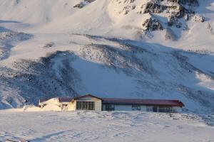 a building in the snow with a snow covered mountain at Steinn Farm Private Apartment in Sauðárkrókur