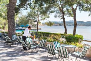 
a man sitting at a picnic table in front of a body of water at Hotel Cala Fornells in Paguera
