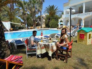 a man and woman sitting at a table by a pool at Alessandro in Sidari