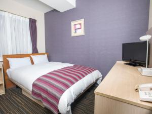 a hotel room with a bed and a desk with a television at FLEXSTAY INN Shinagawa in Tokyo