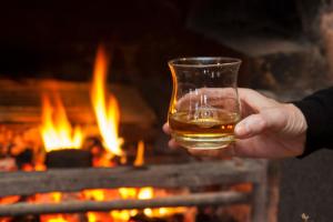 a person holding a glass of whiskey in front of a fireplace at Port Charlotte Hotel in Port Charlotte