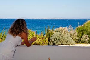 Amarandos Sea View Apartments في Vokaria: امرأة تجلس على الحائط وتطل على المحيط