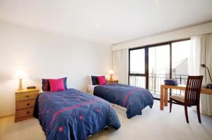 a bedroom with two beds and a desk and a window at Pension Grimus Zurs Suite in Mount Buller