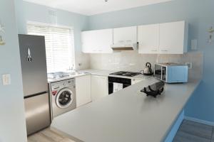 a kitchen with white cabinets and a washer and dryer at Whale View Self Catering Apartment in Hermanus