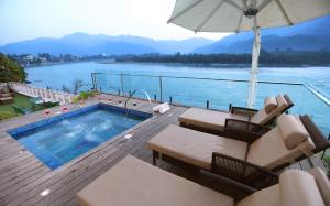 a swimming pool with chairs and an umbrella on a deck at GANGA KINARE- A Riverside Boutique Resort, Rishikesh in Rishīkesh