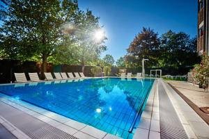 a large swimming pool with chairs and trees at Wellnesshotel Wittelsbach in Bad Füssing