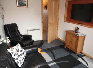 a living room with a black leather couch and a television at Castleyards Apartment 1 in Kirkwall