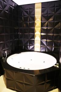 Baño de azulejos negros con bañera blanca en Hotel Años 50, en Torremolinos