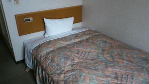 a bed in a hotel room with a pillow on it at Hotel New Budget Sapporo in Sapporo