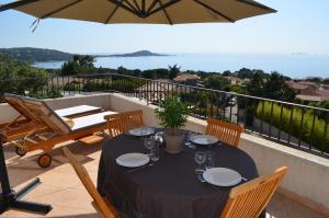 una mesa con sillas y una sombrilla en el balcón en Kallisté Porticcio AppartHotel Golfe d Ajaccio, en Porticcio