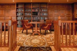 uma biblioteca com cadeiras e uma mesa e estantes em The Glenburn Hotel em Rothesay