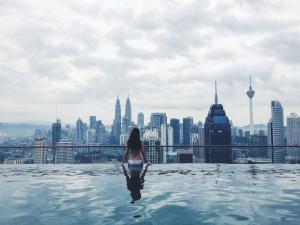 una mujer sentada en una piscina infinita con vistas a una ciudad en Amazing KLCC View @ Regalia Residence, en Kuala Lumpur