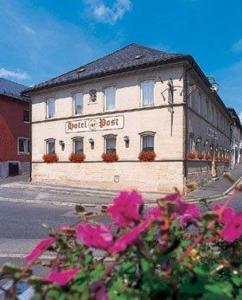 a building on the side of a street with pink flowers at Hotel Post in Nordhalben