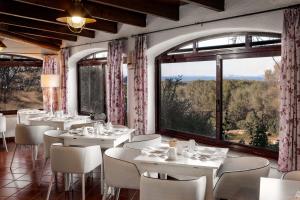 een restaurant met witte tafels en stoelen en grote ramen bij Agriturismo Nuraghe Tuttusoni in Aglientu