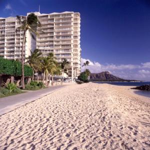 a beach with palm trees and a large building at Waikiki Shore Beachfront in Honolulu